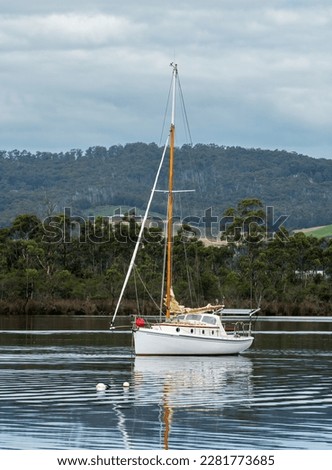A Sailing boat anchored on the Huon River, Tasmania, on a clear morning with reflections.
