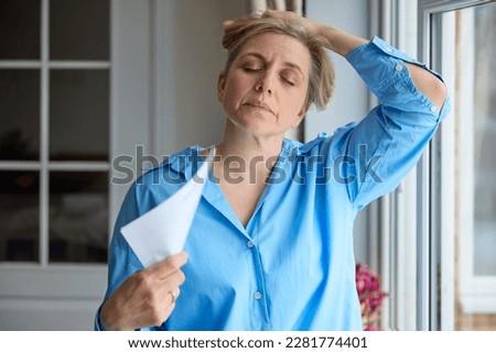 Menopausal Mature Woman Having Hot Flush At Home Cooling Herself With Letters Or Documents Royalty-Free Stock Photo #2281774401