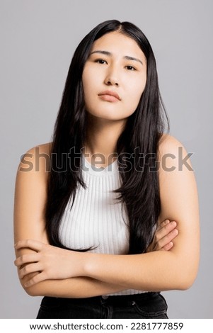 Asian girl in bad mood standing on grey background in studio isolated.
