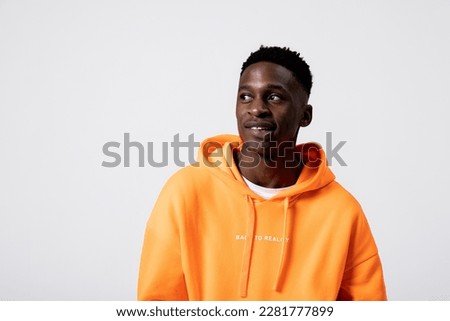 Serious concentrated african american man in orange hoodie looking up at something new advertisement banner happy handsome stylish guy in fashionable clothes standing over grey background in studio. Royalty-Free Stock Photo #2281777899