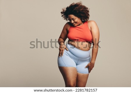 Woman in sportswear showing her physical fitness and flexibility through dance. With a confident expression, she celebrates her fitness journey, proving that body positivity is truly empowering. Royalty-Free Stock Photo #2281782157