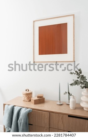 detail in living room with stylish interior, wall decor, eucalyptus branches, candlestick and bamboo jewelry box on wooden chest of drawers