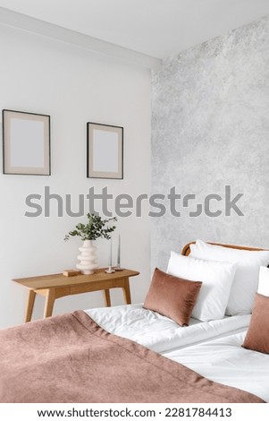 bedroom in apartment with stylish interior, comfortable bed with bedclothes, soft cushions and brown textile cover, wooden table with candles and vase, mockup pictures on wall