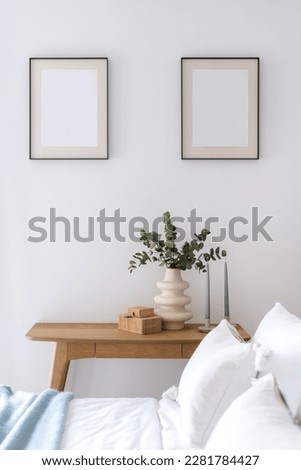 cozy interior in hotel room, view on wooden table with candles, eucalyptus branch in ceramic vase, jewelry box and pictures in frame on wall through bed with bedding