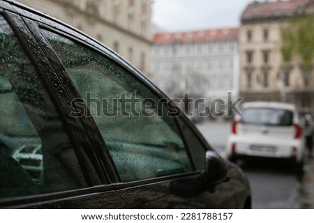 Car window and blurred city background. Cityscape backdrop. Cloudy rainy weather. Green city concept and reduce carbon footprint.