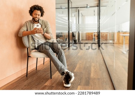 Trendy manager holding smartphone in hands, male office employee using phone for chatting online, messaging. Freelancer guy using phone for working