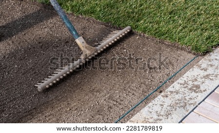 Preparing the soil with a rake for new turf and laying a cable for an automatic lawn mower robot near the terrace Royalty-Free Stock Photo #2281789819