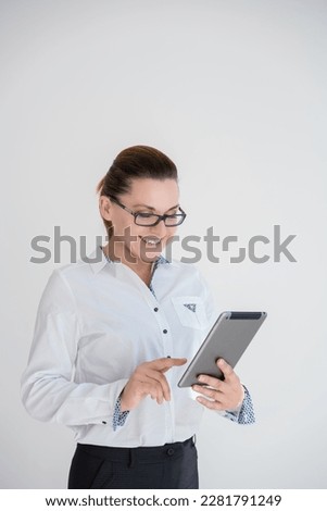 Image of young caucasioan woman in black costume wearing eyeglasses, company worker in glasses, smiling and holding digital tablet, standing over white background. Concept of success and technology.