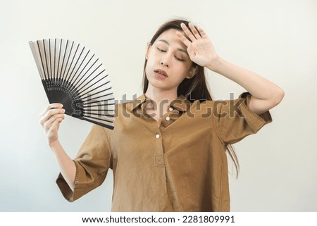 Suffering summer heat stroke, hot weather, tired asian young woman, girl sweaty and thirsty, refreshing with hand in blowing, wave fan to ventilation when temperature high at home, house on background Royalty-Free Stock Photo #2281809991