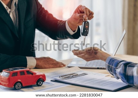 Explain promotions and car insurance for rental or purchase. A car dealer or sales manager hands the keys to the car owner and explains the terms of the car contract at a desk in the office.