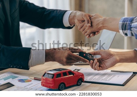 Explain promotions and car insurance for rental or purchase. A car dealer or sales manager hands the keys to the car owner and explains the terms of the car contract at a desk in the office.
