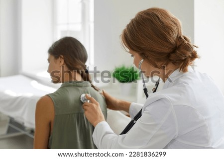 Doctor with a stethoscope examining a child patient. Female doctor in a white coat examining the lungs of a teenage girl. Healthcare, clinic, medical checkup concept Royalty-Free Stock Photo #2281836299