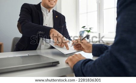 Two happy young people make a business deal and sign a contract agreement in the office. Friendly, smiling agent shows his client where to put a signature. Cropped shot. Banner background