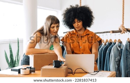 Thrift store owners having a discussion while using a laptop in their shop. Two small business owners preparing parcels for shipping. Female entrepreneurs running an online clothing store. Royalty-Free Stock Photo #2281837413