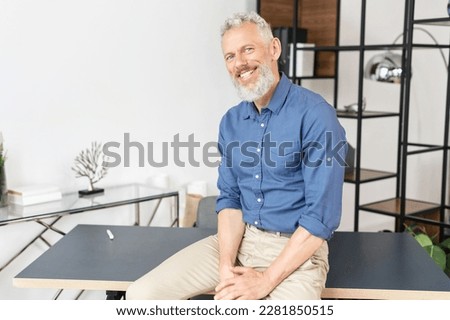Successful senior business owner in casual wear indoors. Handsome charismatic mature man leaned on the desk and looks at the camera with a smile Royalty-Free Stock Photo #2281850515