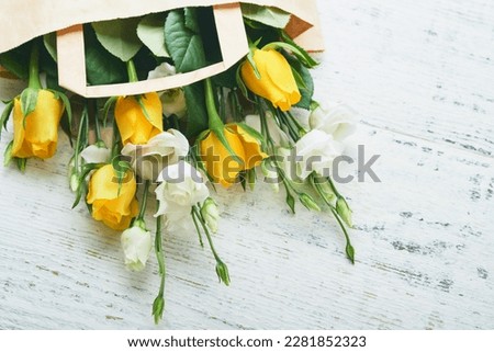 Easter concept. Bouquet of fresh white and yellow roses in paper bag on old white wooden background. Passover Pesah celebration concept. Concept of mothers day, womens day, spring background. Top view