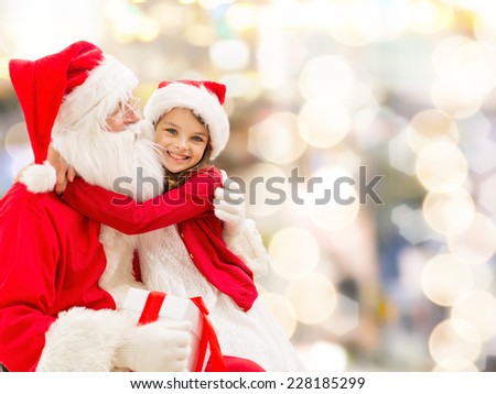 holidays, christmas, childhood and people concept - smiling little girl hugging with santa claus over lights background