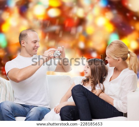 family, holidays, technology and people - smiling mother, father and little girl with camera over red lights background