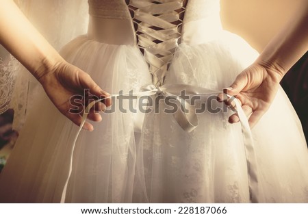 Closeup toned photo of beautiful bride tying up her wedding dress Royalty-Free Stock Photo #228187066