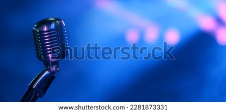 Vintage vocal microphone on concert stage with blue and pinks spotights. Wide panoramic background for music festival, podcast or jazz club website with copy space.