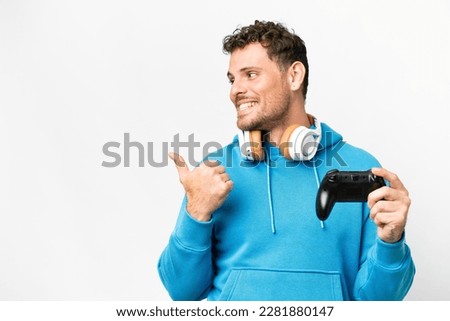 Brazilian man playing with a video game controller over isolated white background pointing to the side to present a product