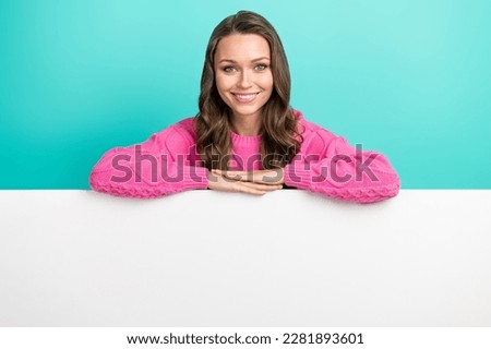 Photo of cheerful positive girl wear pink sweater holding arms holding poster empty space isolated turquoise color background