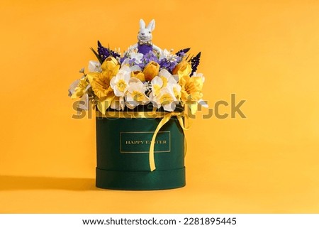 Easter decoration with beautiful spring flowers in box, Easter eggs and bunny on yellow background. Festive concept with copy space.