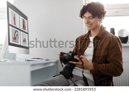 Photographer looking at photos on his DSLR camera, sitting at table with computer, man working with post processing editing software on modern desktop