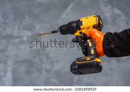 Male worker holds a close-up electric cordless screwdriver in his hands against the background of a construction tool and a concrete wall