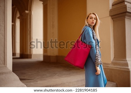 Fashionable blonde woman wearing trendy outfit with blue coat, zebra print scarf, fuchsia color faux leather tote, shopper bag, posing in street. Copy, empty space for text Royalty-Free Stock Photo #2281904185