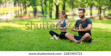 Full body image - smiling couple  sitting in lotus position or woman practicing with man, male bearded coach trainer doing yoga exercises, meditating together, after outside training. Wide composition