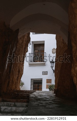 Small passageway that crosses under the rock of the castle of Guadalest, in Alicante, with a typical house with a white facade in the background