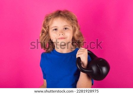 Kid with kettlebell in studio on red pink background. Cute child boy pumping up arm muscles with dumbbell. Fitness kids with dumbbells.