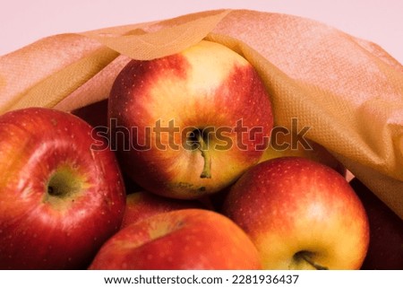Red apples in a reusable fruit and vegetable bag on a pink paper background. Concept of earth day, zero waste and recycling.