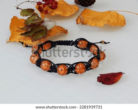 Orange friendship bracelet on a white. Orange bracelet and leafs