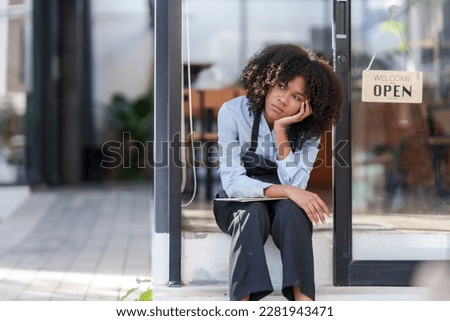 Female shopkeeper sitting stressed out at the store entrance frustrated by the economic impact. Royalty-Free Stock Photo #2281943471