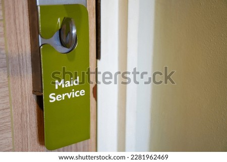 A close-up view of a hotel maid service tag hanging on a doorknob with copy space, signaling the need for a room clean