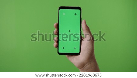 Close up of man's hand holding a smart phone with vertical green mock up chroma key screen and doing gestures on touchscreen 