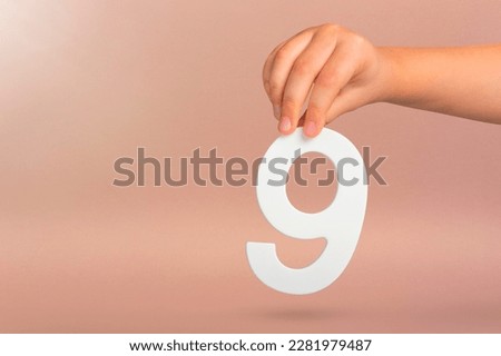 Number nine in hand. A hand holds a white number 9 on a red background. Concept with number nine. Birthday 9 years, percentage, ninth grade or day. Royalty-Free Stock Photo #2281979487
