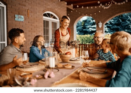 Happy woman serving food to her extended family at dining table on a terrace.