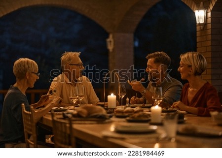 Senior couple talking to their son and his wife while eating dinner at dining table on a terrace. 