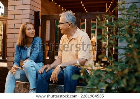 Happy teenage girl and her grandfather communicating on while sitting on staircase on a patio.