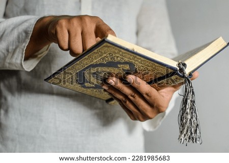 Holy Quran in Hand with arabic calligraphy meaning of Al Quran. Muslim man pointing the finger on holy Quran and reading it. Royalty-Free Stock Photo #2281985683