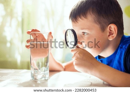 The child boy looking at water in a glass through magnifying glass Royalty-Free Stock Photo #2282000453