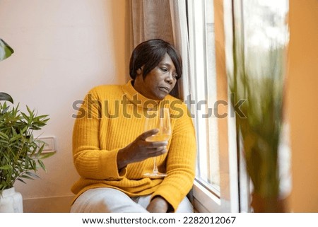 African American mature woman, drinks wine by the window. alcoholic, depressed, sad woman. Royalty-Free Stock Photo #2282012067
