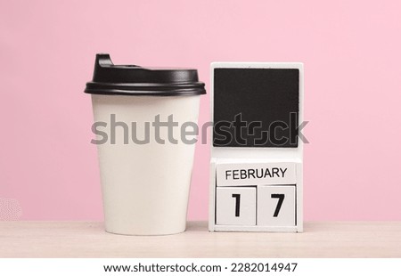 White wooden block monthly calendar with the date february 17 and coffee cup on the table, pink background. Planning, business concept