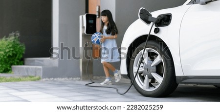A playful and happy girl playing around at her home charging station providing a sustainable power source for electric vehicles. Alternative energy for progressive lifestyle.