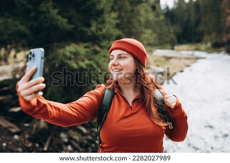 Woman in hat uses a telephone for take pictures, makes selfies and video calls family from home on mountains background. Travel and wanderlust concept. Amazing chill moment