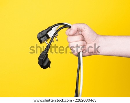 A male hand holds three electric plugs. No face, yellow background, copy space.
 Royalty-Free Stock Photo #2282030463