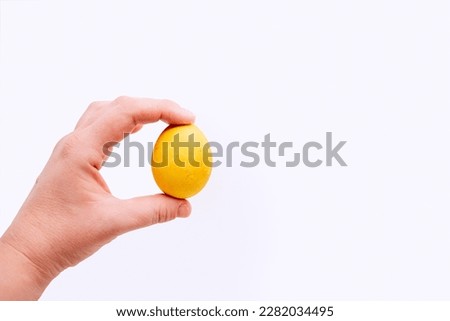 Human hand holds orange, deep yellow Easter egg on an isolated white background. Place for text. Mock up, copy space. Minimalism